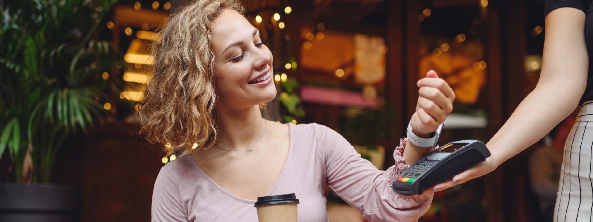 Imagem exibe mulher sorridente realizando pagamento por aproximação com smartwatch.