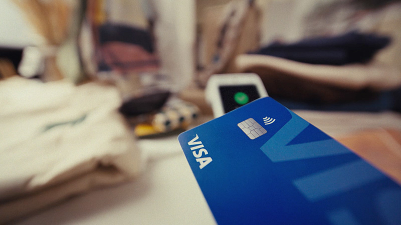 Close-up of a blue Visa contactless credit card being tapped on a payment terminal.